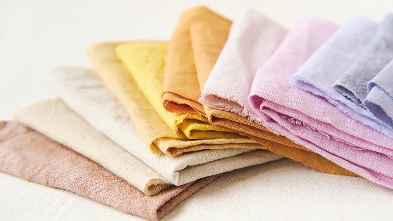 Stack of naturally dyed linen fabric in soft pastel and earthy tones.