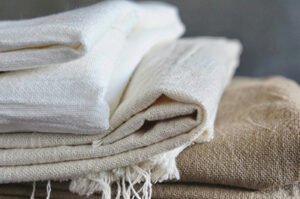 Stack of neatly folded natural and off-white linen fabrics in various textures.