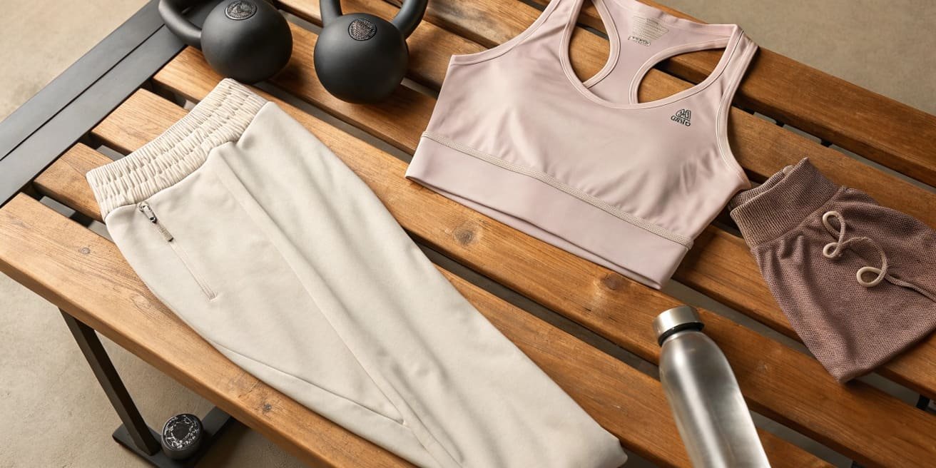 Sports bra, joggers, shorts, and gym gear on wooden bench.
