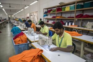 Workers sewing colorful garments in a factory with neatly stacked fabric in the background