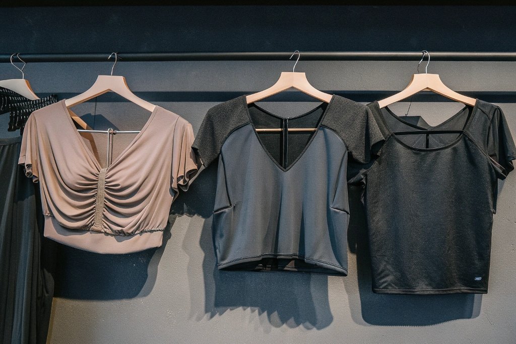 Three stylish women’s tops in neutral colors hanging on wooden hangers.
